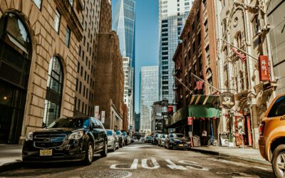 looking down a street in newyork with cars parked on the left and colourful storefronts to the right of the image